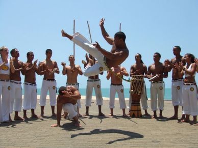 Group practicing Capoeira outdoors under clear sky.