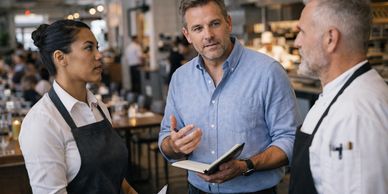 Manager discusses with two restaurant staff members during a meeting.