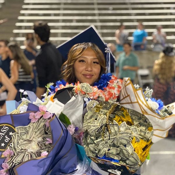 A graduate smiling with money bouquets and leis around her neck.
