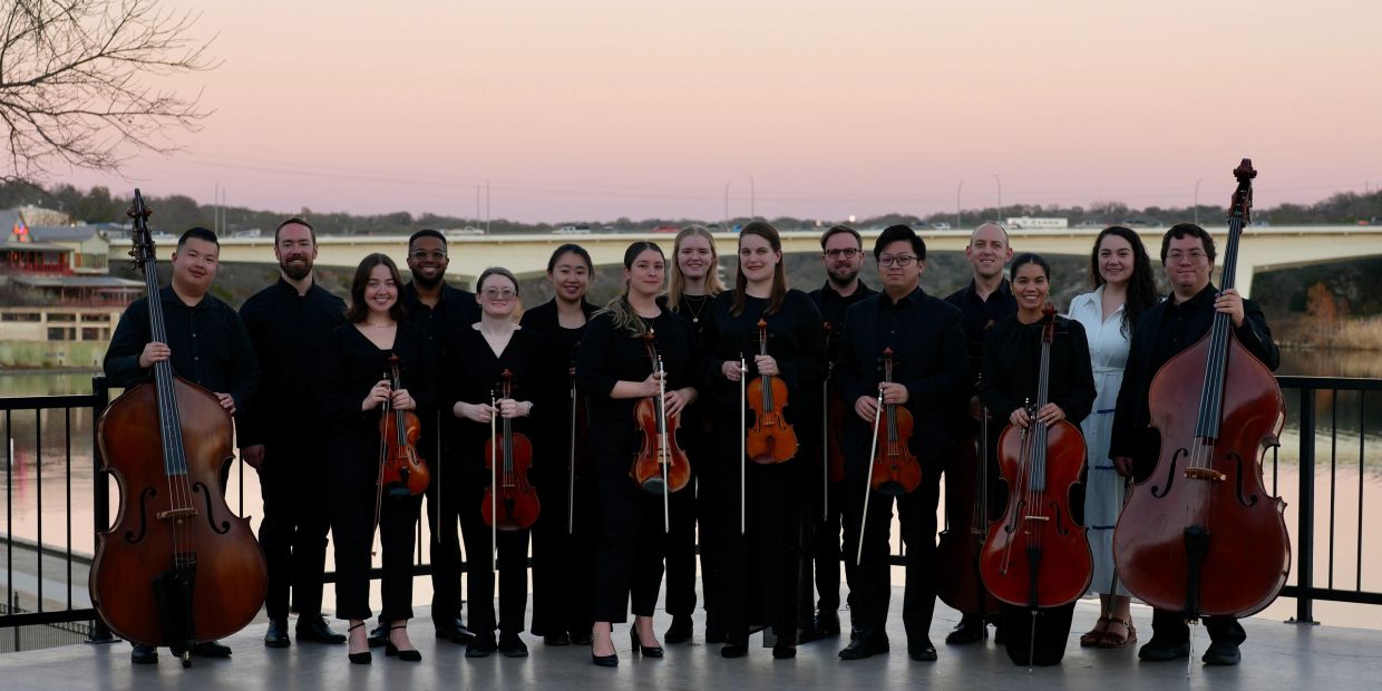 Group portrait of musicians with string instruments by a riverside at dusk.