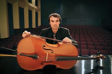 Musician with cello on a stage in an empty auditorium.