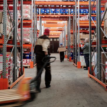 Workers moving boxes in a warehouse aisle.