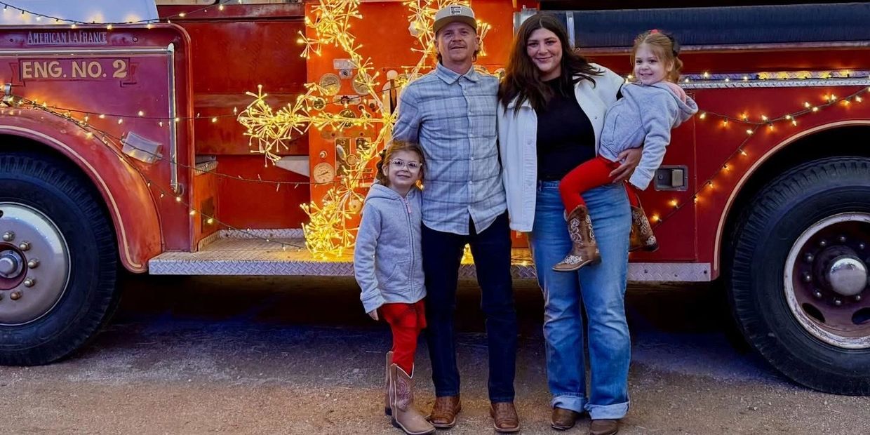 Family posing in front of a decorated vintage fire truck with lights.