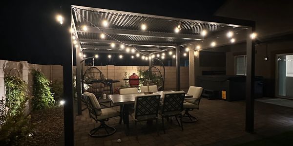 Illuminated backyard patio with string lights and outdoor furniture at night.