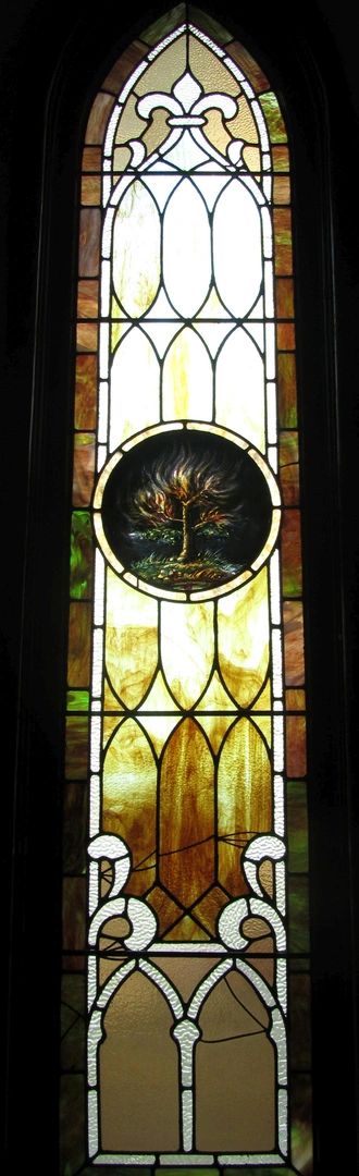 Tall stained glass window with a flaming tree centerpiece and geometric patterns.