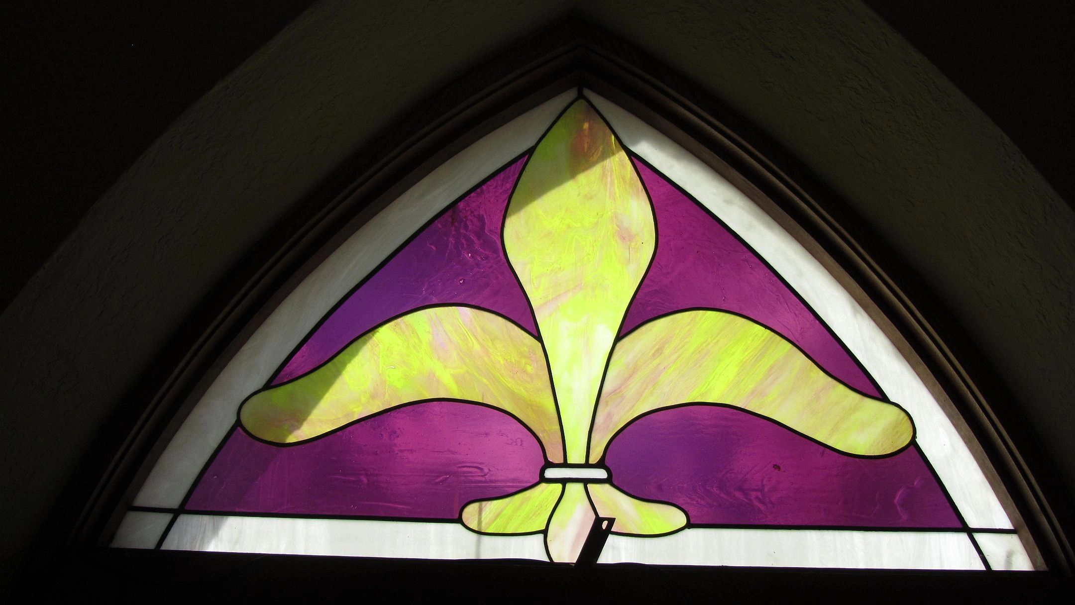 A stained glass window featuring a yellow fleur-de-lis on a purple background.