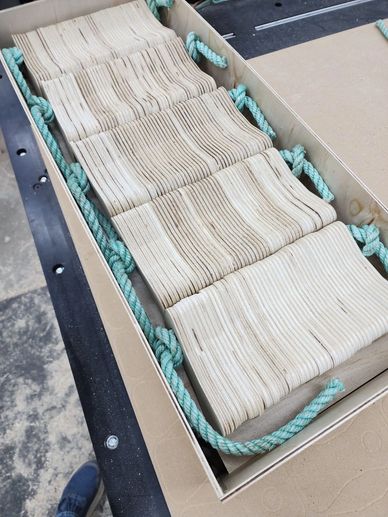 Rows of wooden blocks neatly arranged in a cardboard box with blue rope handles.