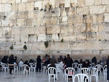 People praying and sitting by the Western Wall in Jerusalem.