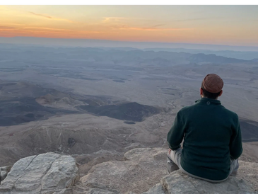 Person sitting on a rock overlooking a vast desert at sunset.