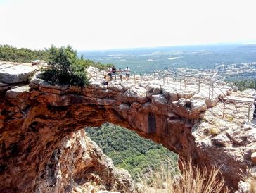 People stand on a rocky natural bridge overlooking a forested valley and distant town.