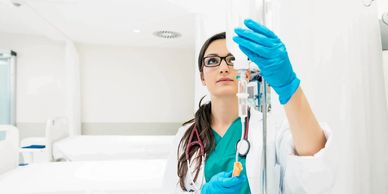 Female healthcare professional adjusting an IV drip in a hospital room.