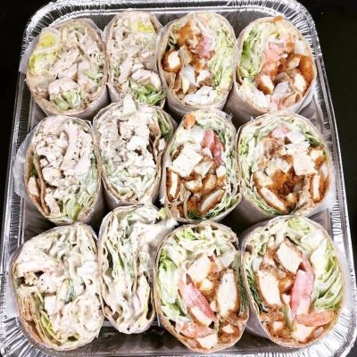 Tray of assorted chicken wraps with lettuce and tomato.