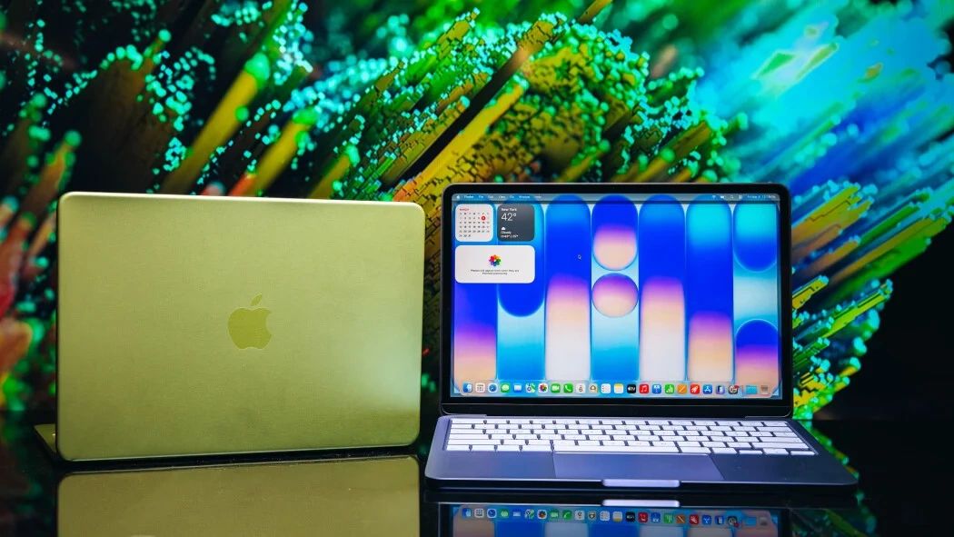Two Apple MacBook laptops, one closed and one open, on a reflective surface.