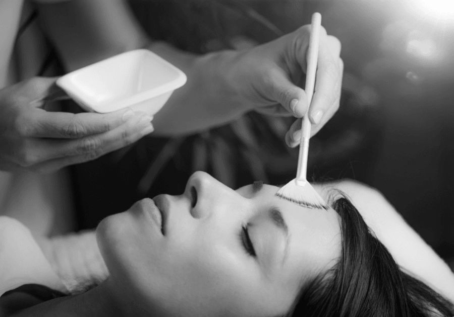 Black and white image of an esthetician applying a chemical peel treatment to the face.