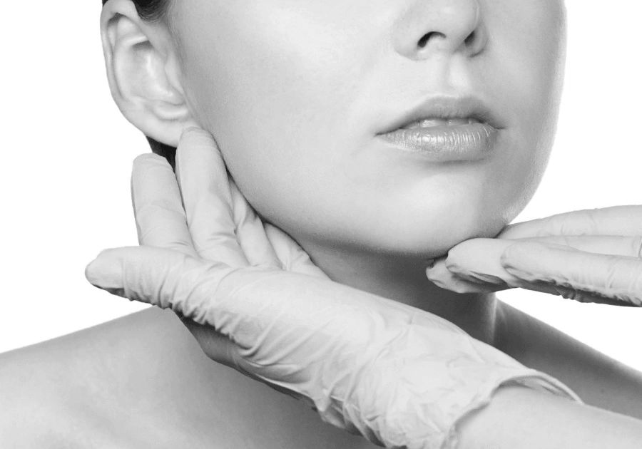 Black and white close-up of gloved hands gently supporting the face during a skin consultation.