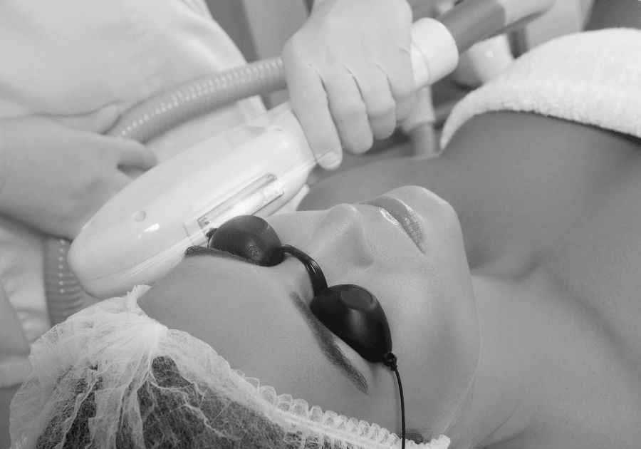 Black and white image of an esthetician performing an IPL light treatment on the face.