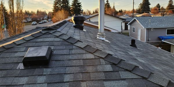 View of a rooftop with vents and nearby houses in the evening.