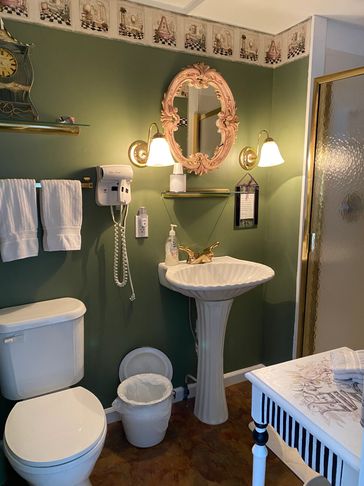 Cozy bathroom featuring green walls, vintage decor, a pedestal sink with a gold faucet