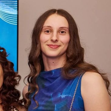 Young woman with long curly hair smiling, wearing a blue dress.