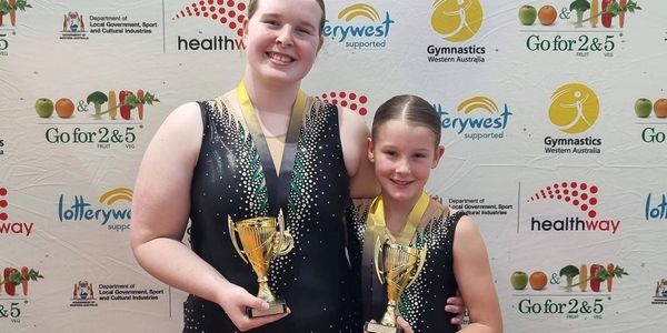 Two gymnasts holding trophies and wearing medals.