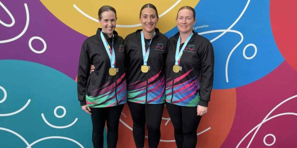 Three women with gold medals posing in matching jackets.