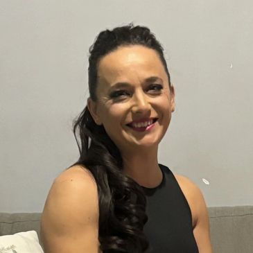 Smiling woman with long dark hair in a black sleeveless top against a plain background.