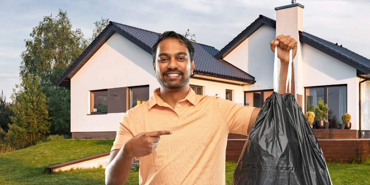 A man of South Asian descent holds a small bag of trash, pointing to it with his other hand, while s