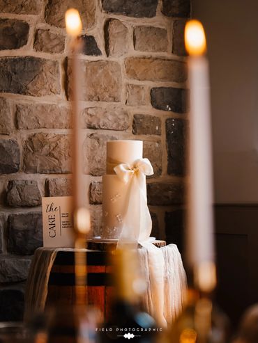 2 tier extended height white cake with floral appliqué and oversized ribbon details. 