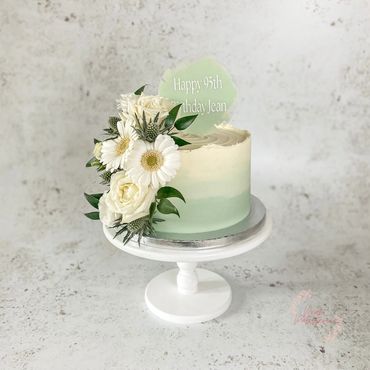 Sage green and white ombré cake with fresh floral arrangement and 95th birthday cake paddle