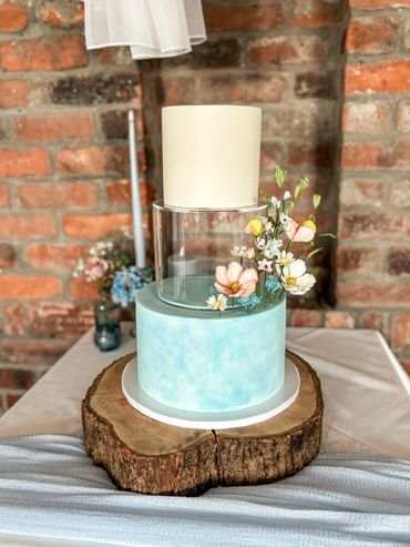 3 tier wedding cake with clear spacer tier, textured dusky blue and white with sugar flowers.
