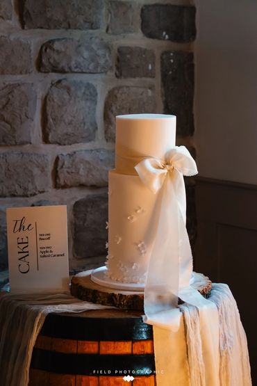 2 tier extended height white cake with floral appliqué and oversized ribbon details.  