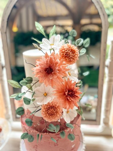 Close up of orange sugar dahlias, white sugar cosmos and sugar eucalyptus on a 3 tier cake.