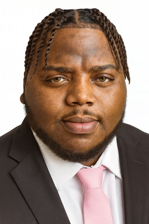 Close-up portrait of a man with braided hair, beard, and a pink tie.