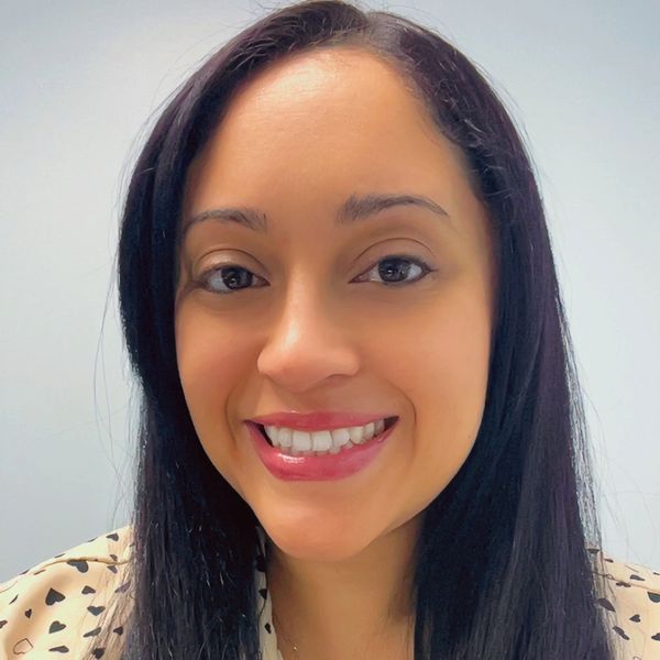 Smiling woman with long black hair wearing a heart-patterned blouse.