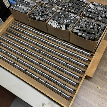Rows of cylindrical metal parts organized in a wooden tray and boxes.