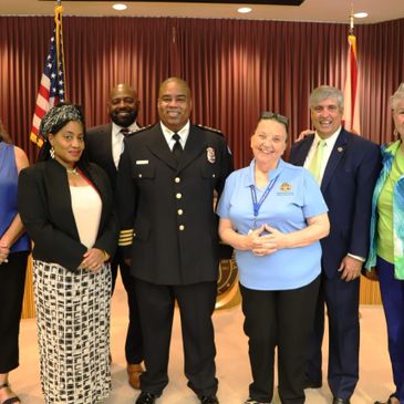 Group of professionals posing with a fire chief in an official setting.