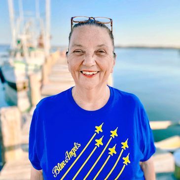 Smiling woman wearing a Blue Angels t-shirt near water.