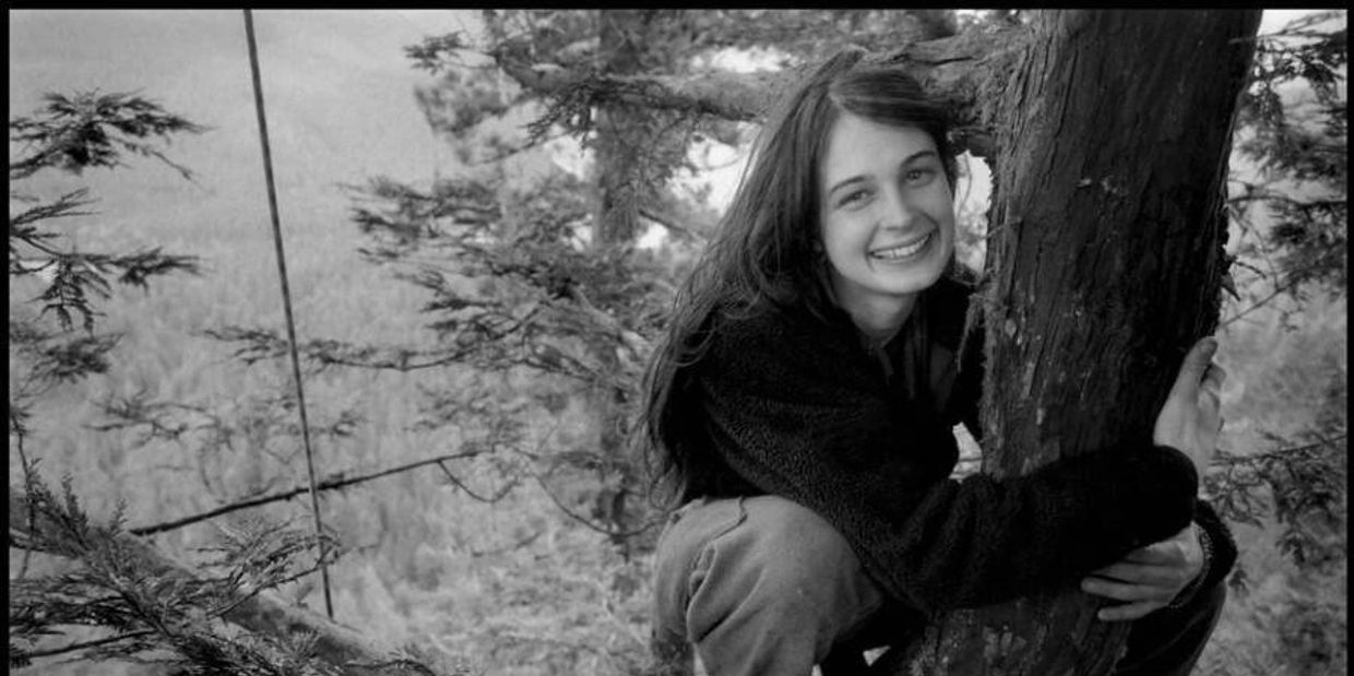 Smiling woman hugging a tree in a forest, black and white photo.