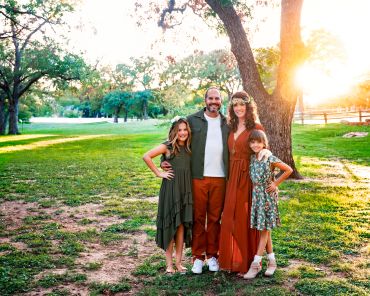 A family of four posing outdoors by a tree at sunset.