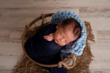 Newborn baby sleeping peacefully in a basket with blue blanket.