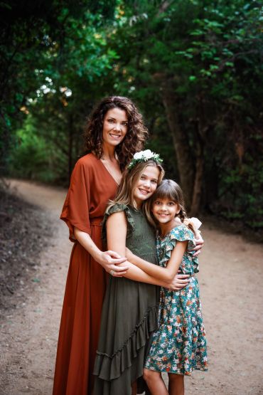 Woman and two girls embracing outdoors on a forest path.