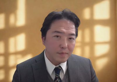 Man in a suit posing against a softly lit window background.