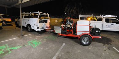 Work trucks and equipment parked under a shelter at night.