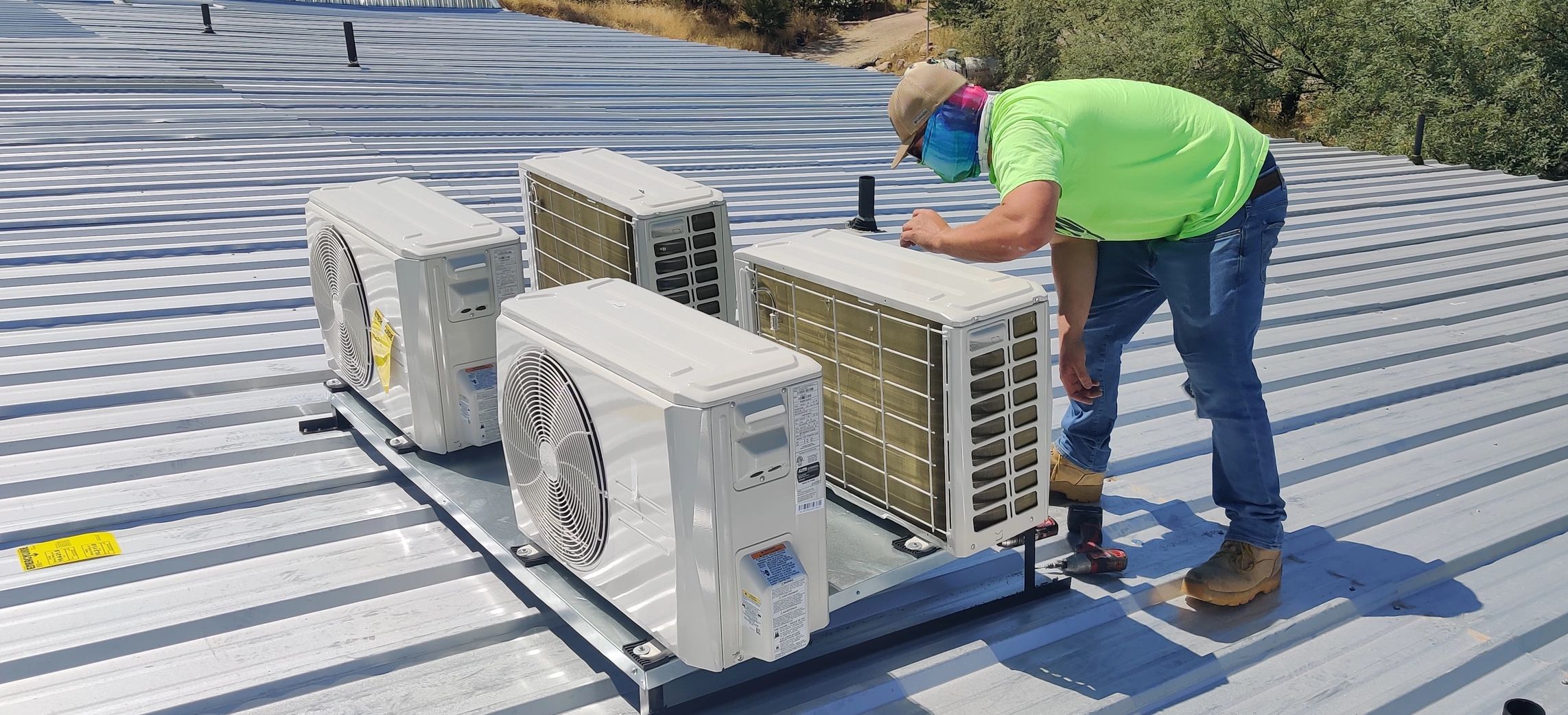 Technician inspecting rooftop air conditioning units on a metal roof.