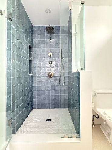 Modern bathroom with blue tiled shower and glass door.