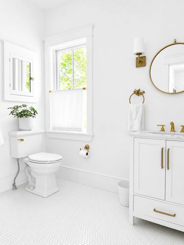 Bright white bathroom with gold accents and natural light from window.