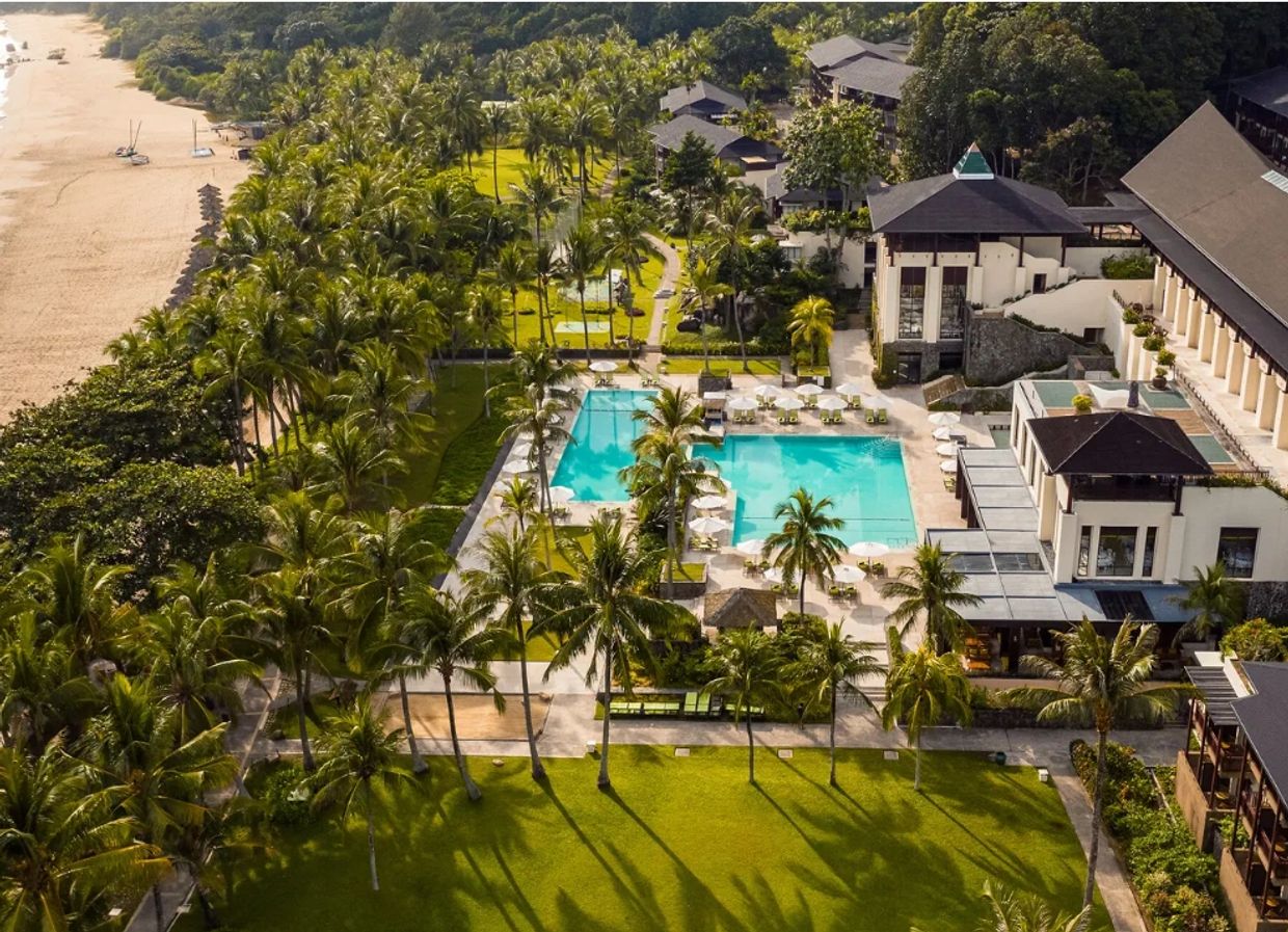Aerial view of a tropical resort with a pool, palm trees, and a nearby beach.