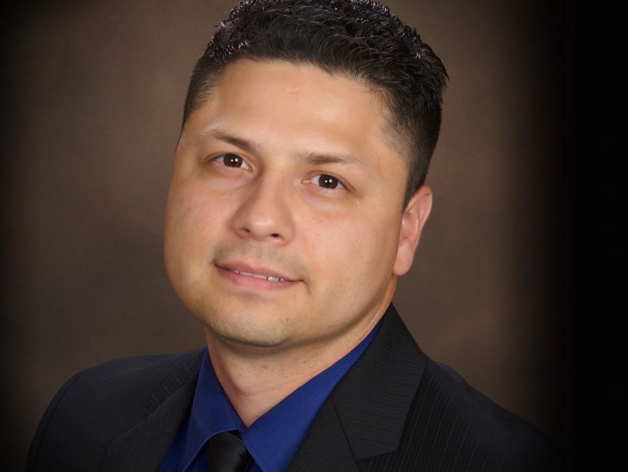 Professional headshot of a man in a suit and blue shirt.