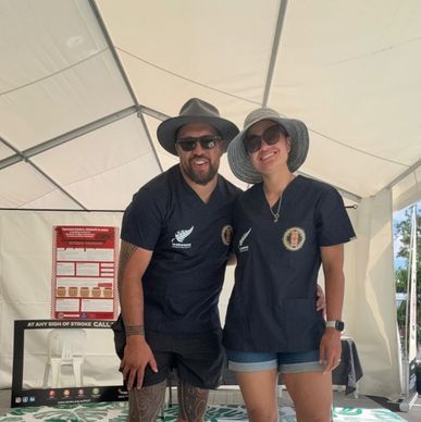 Two people in hats and navy shirts smiling under a tent.