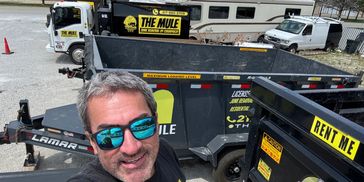 Man takes selfie wearing sunglasses and The Mule junk removal shirt near trailers and truck.